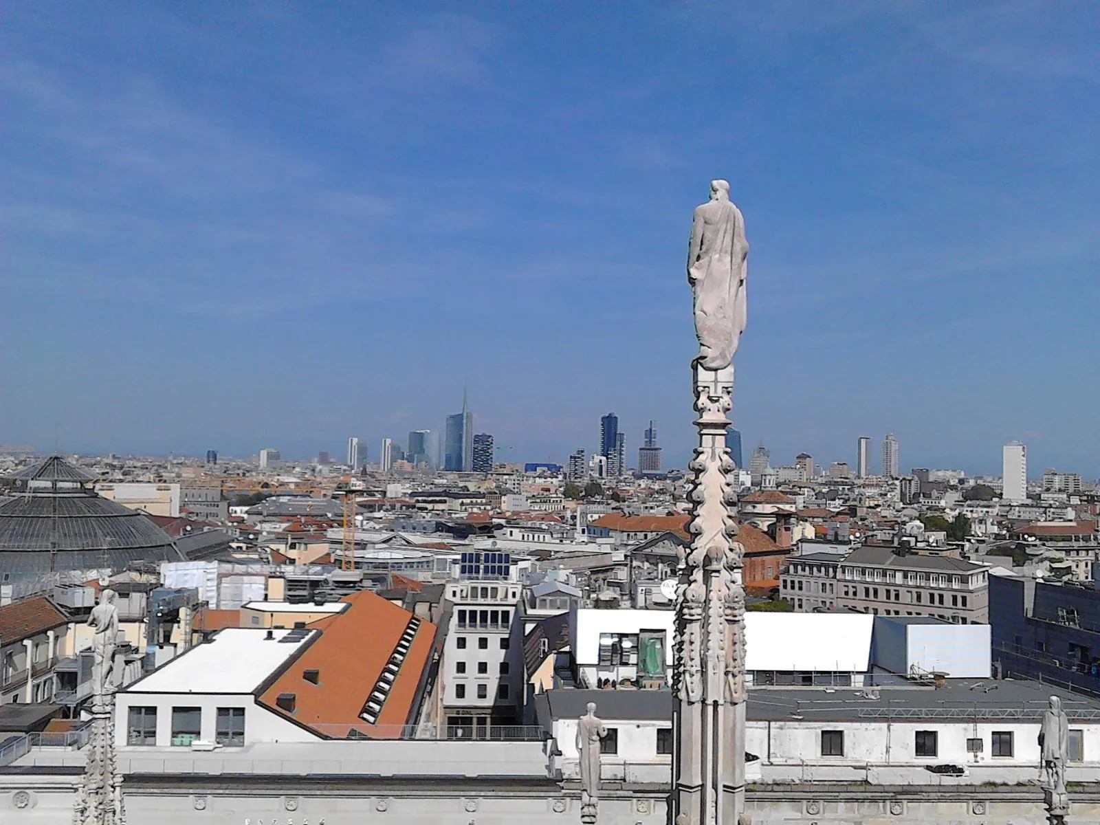 Vista panoramica di Milano dalle terrazze del Duomo verso i grattacieli di Porta Nuova, con una statua di guglia in primo piano